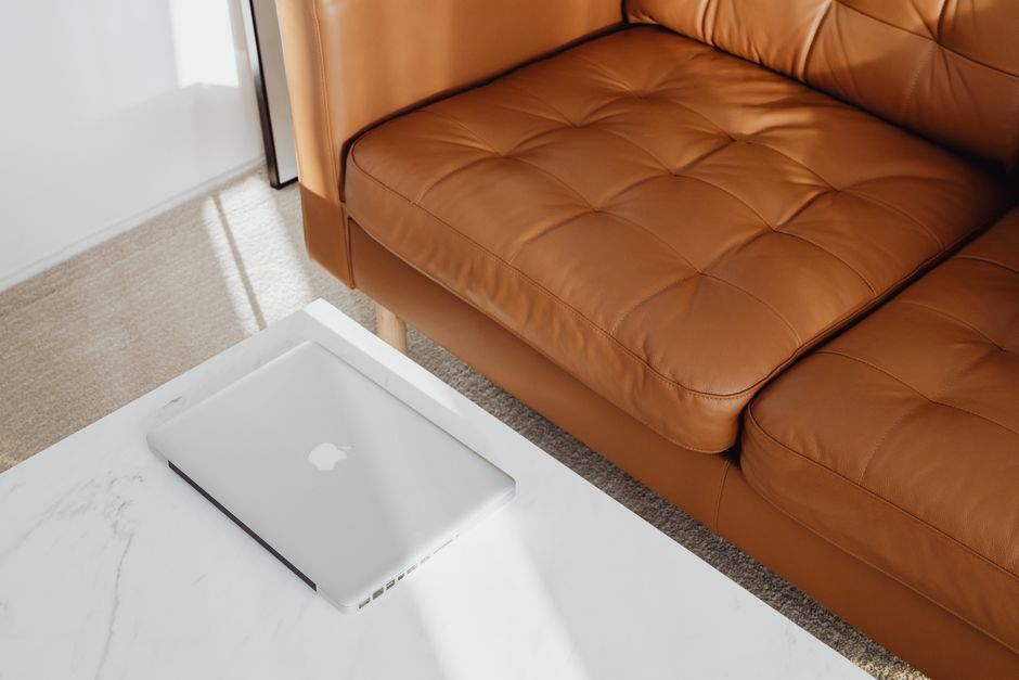 Stylish living room featuring a brown leather couch and laptop on a marble table.
